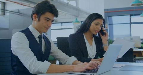Business colleagues collaborating, reviewing documents on laptop and phone in modern office