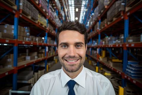 Confident Warehouse Manager Smiling in Organized Inventory Aisle