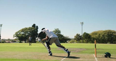 Hispanic batsman tapping bat and shifting stance at crease while bowler readying delivery