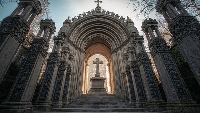 Gothic archway framing latin cross on stone steps at urban memorial, ornate columns