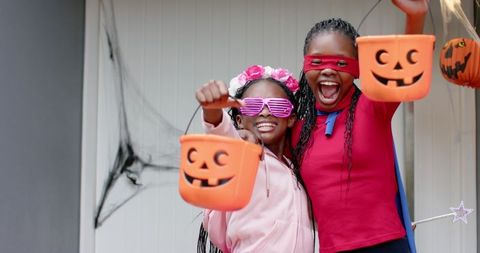 African american girls celebrating halloween trick-or-treat with pumpkin buckets, costumes