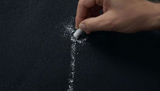 Hand placing white chalk granules into precise line on blackboard closeup for texture