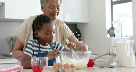 African american grandmother teaching granddaughter baking in bright kitchen