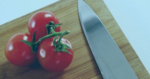 Three Cherry Tomatoes on Vine Sitting beside Serrated Knife on Bamboo Cutting Board