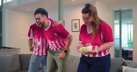 Friends cheering and reacting in living room wearing red and white team jerseys