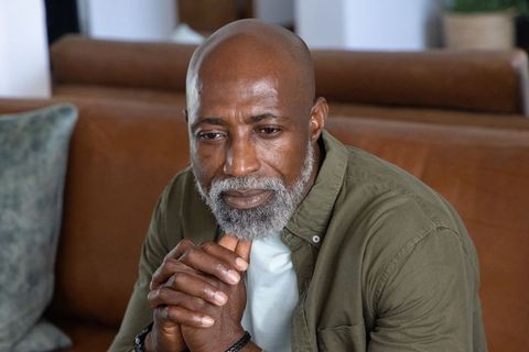 Contemplative mature african man sitting on brown sofa reflecting on life and solitude