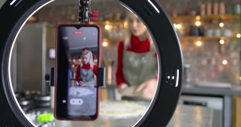 Home cook filming baking tutorial with ring light and smartphone kneading dough
