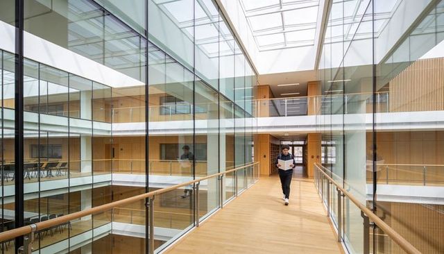 Male student walking on glass atrium walkway reading papers under skylight at university