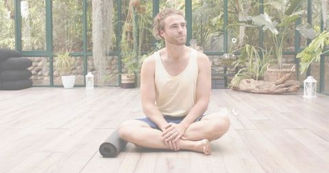 Sunlit greenhouse yoga: man sitting cross-legged meditating with rolled mat