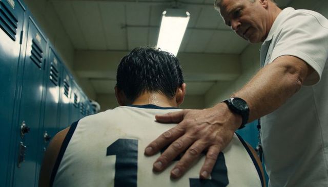 Coach comforting slumping basketball player in locker room after tough game