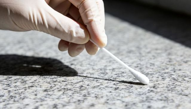Collecting environmental swab sample with nitrile-gloved hand on granite countertop