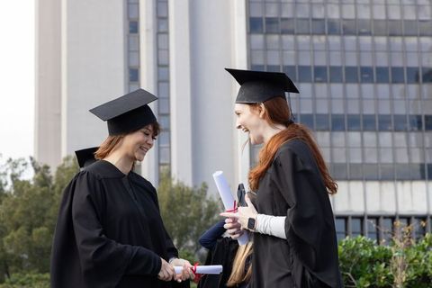 Diverse female graduates exchanging diplomas and celebrating together on university campus lawn