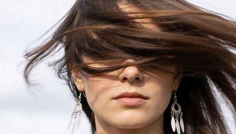 Wind-swept hair covering eyes woman wearing boho silver earrings outdoor close-up portrait