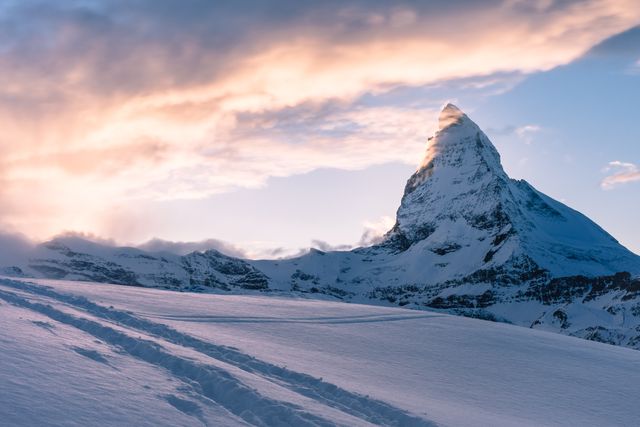 Beautiful sunset view of a snow-covered mountain peak with fresh track marks in the foreground. Perfect image to showcase adventure, outdoor activities, hiking, winter scenery, travel destinations in nature, and snow sports.