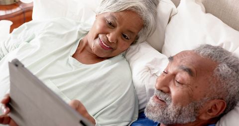 Happy senior couple engaged on tablet in bed