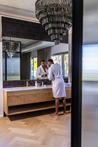 African american man grooming at vanity in modern marble bathroom with chandelier at home