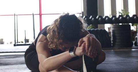 Focused female athlete stretching on gym floor near weights