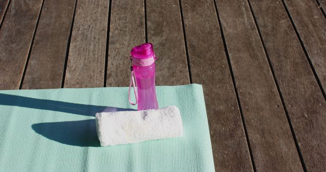 Water bottle, towel and yoga mat on sunny wooden deck outdoors, copy space, slow motion. Yoga, wellbeing, fitness and healthy lifestyle.