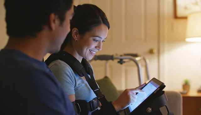 Woman wearing shoulder brace tapping tablet while seated with partner and rollator