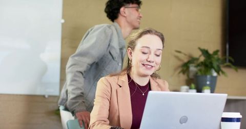 Young professionals collaborating in modern office, woman working on laptop with coffee cup