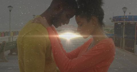 Couple touching foreheads on pier embracing intimacy with soft sunflare and muted tones