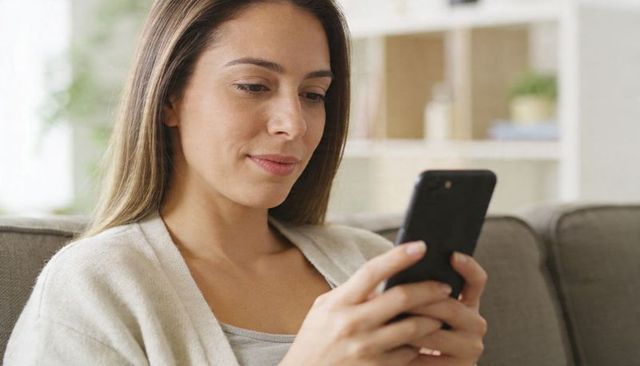 Adult woman scrolling smartphone on sofa wearing beige cardigan relaxed home lifestyle