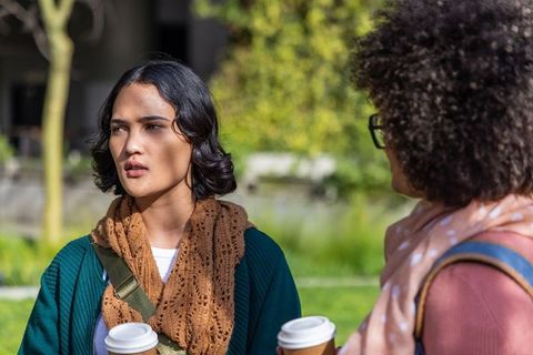 Two women talking and holding takeaway coffee cups in urban park greenspace