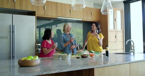 Multicultural friends preparing salad and enjoying wine on marble kitchen countertop