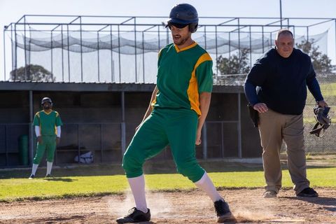Baseball player sliding into home plate with umpire and teammates in green-yellow uniform
