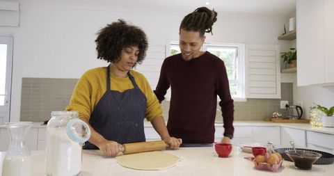African american couple baking together rolling dough on bright modern kitchen island