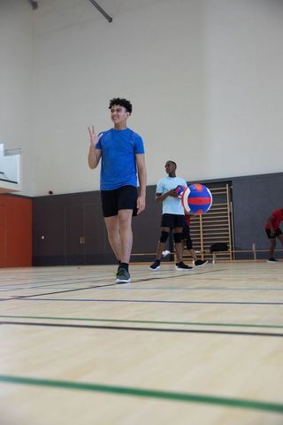 Multicultural teenage teammates walking toward camera holding volleyball in indoor gym
