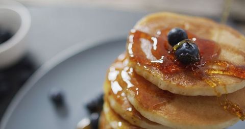 Stack of pancakes dripping with syrup and fresh blueberries top view