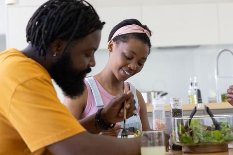 African american couple sharing fresh salad at kitchen table, casual home dining moment