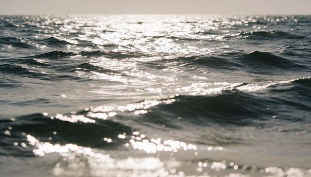 Sunlight sparkling on rolling ocean waves at horizon - calm sea surface with reflections