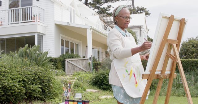 Happy senior african american woman painting picture in garden and smiling, copy space. Retirement, creativity, hobbies and senior lifestyle, unaltered.