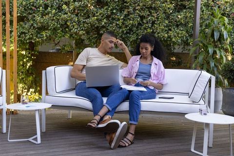 Young diverse coworkers collaborating outdoors on white sofa with laptop and documents