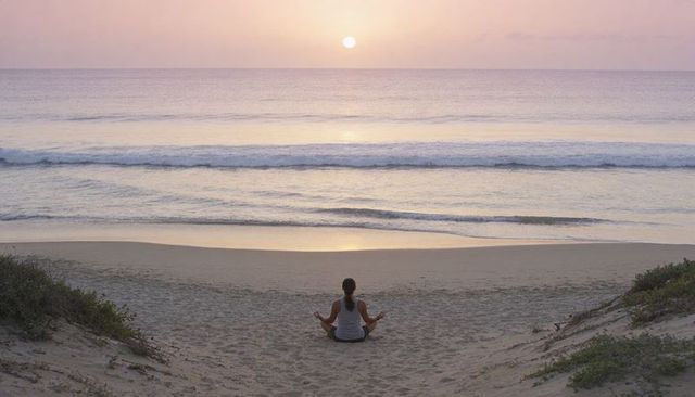 Woman meditating on beach at sunrise with pastel sky and calm ocean