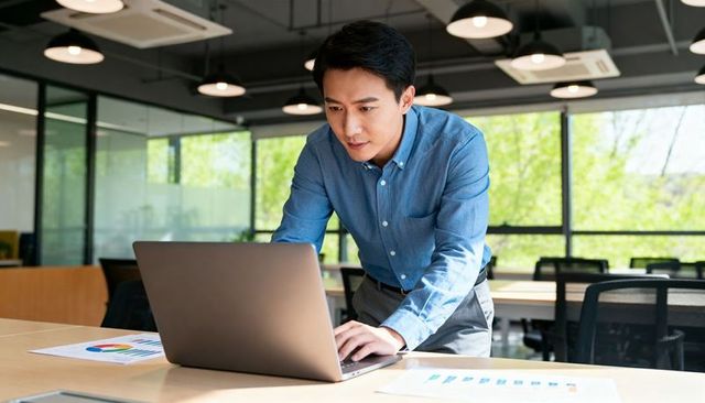 Leaning office professional reviewing charts on laptop in bright modern workspace