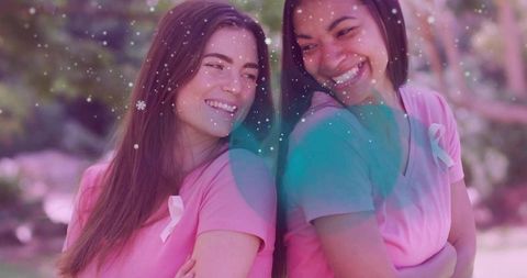 Smiling women leaning back-to-back wearing pink ribbons raising breast cancer awareness