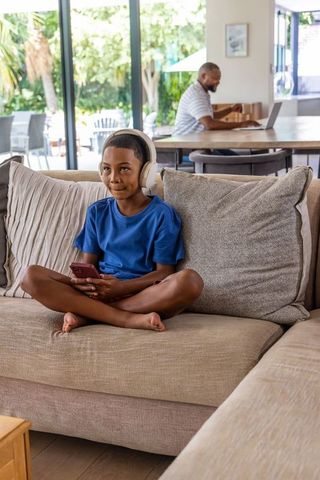 Sunlit family moment: african american dad working while son listening with headphones