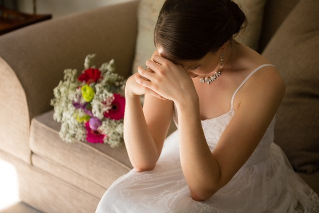 High angle view of upset bride sitting by bouquet on sofa at home