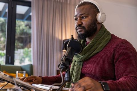 African american man recording podcast in cozy home studio with headphones and microphone