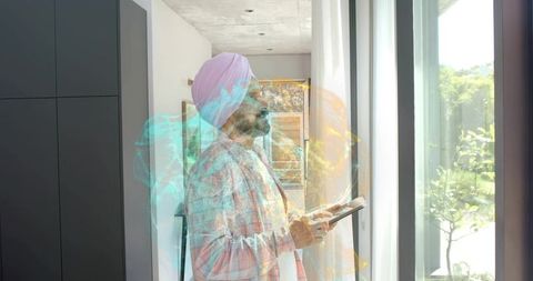 Man wearing pink turban using tablet by floor-to-ceiling windows with holographic overlay