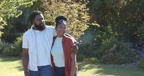African american couple walking arm in arm in sunlit garden smiling and embracing