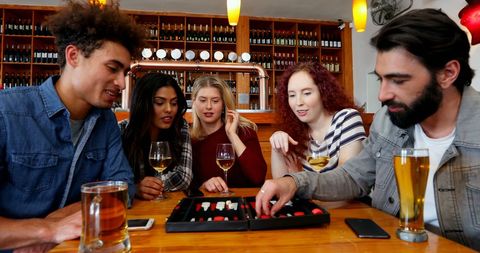 Friends Enjoy Board Game Night at Cozy Bar with Drinks