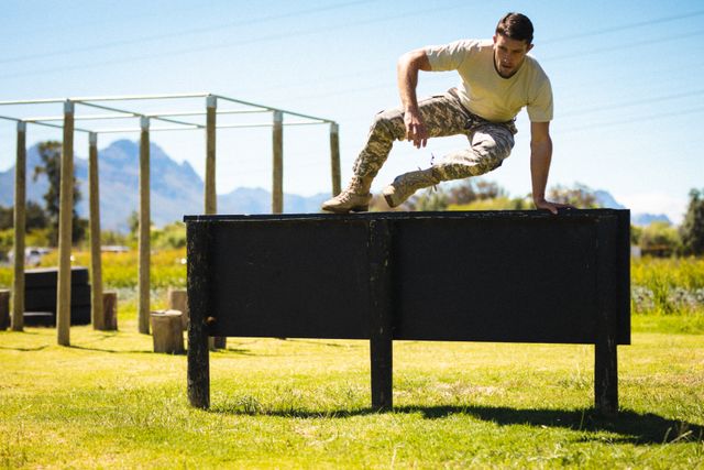 Young male soldier in uniform crossing a hurdle during bootcamp training. Ideal for illustrating military training, physical fitness, endurance, and discipline. Useful for articles, blogs, and advertisements related to military recruitment, fitness programs, and outdoor training activities.