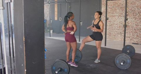 Female trainer coaching trainee in industrial gym with loaded barbells and exposed brick