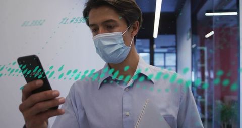 Businessman wearing mask checking phone while holding laptop with teal data overlay