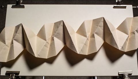 Accordion-folded beige paper casting dramatic zigzag shadows on white board for design