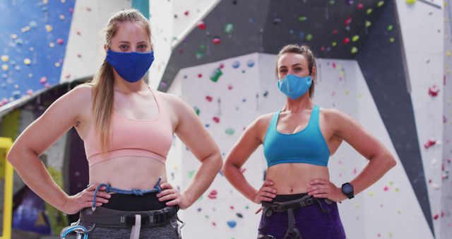 Portrait of two caucasian women wearing face masks standing at indoor climbing wall. fitness and leisure time during coronavirus covid 19 pandemic.